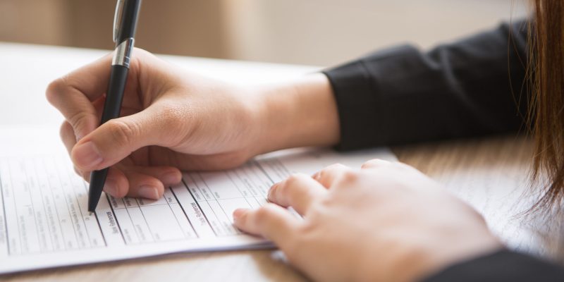 Cropped view of woman holding pen and filling in application form at table